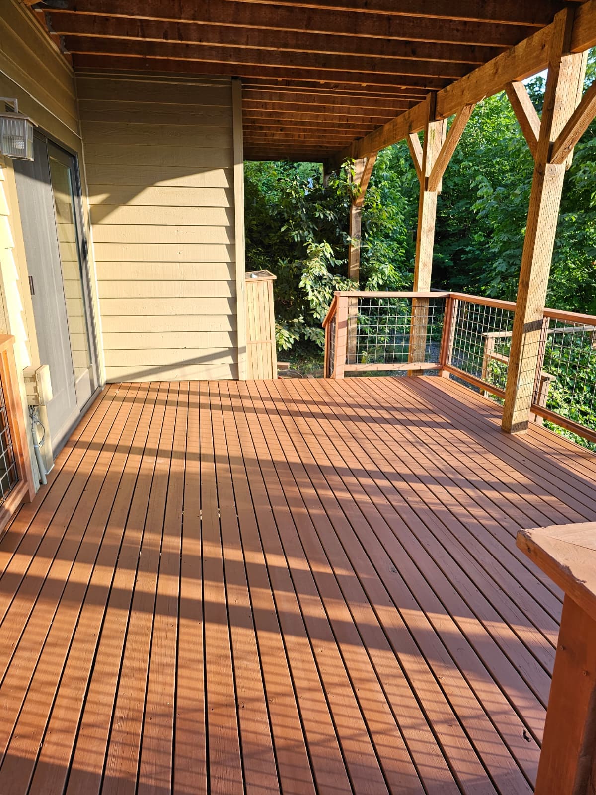 Covered cedar deck freshly stained a warm brown, with timber posts and cable railing