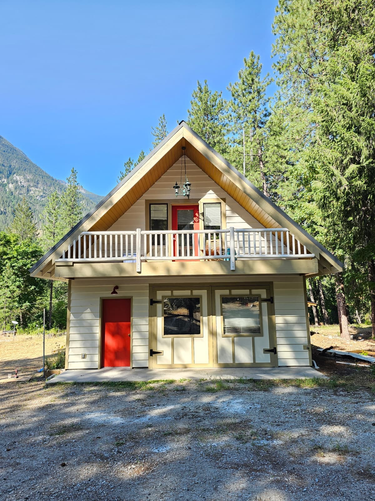 A-frame cabin painted cream with a red front door and a white balcony rail