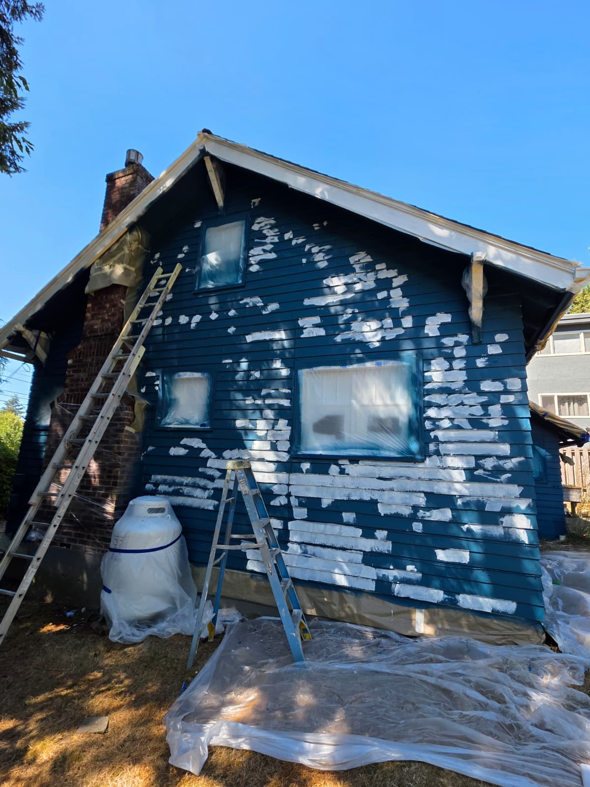 Craftsman exterior mid-repaint, siding spot-primed and windows masked before the finish coats