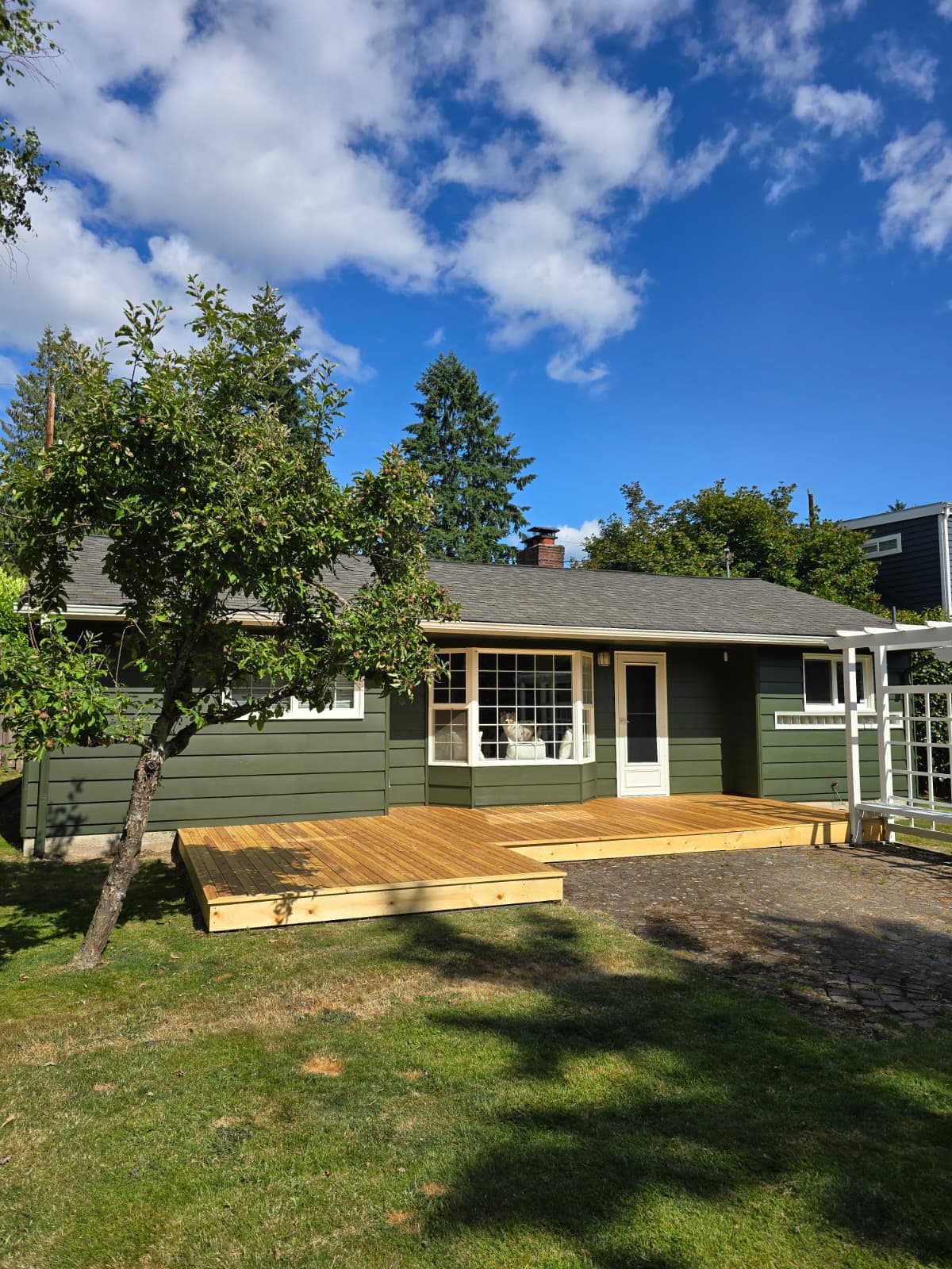 Single-story house painted sage green with a newly built and stained front deck