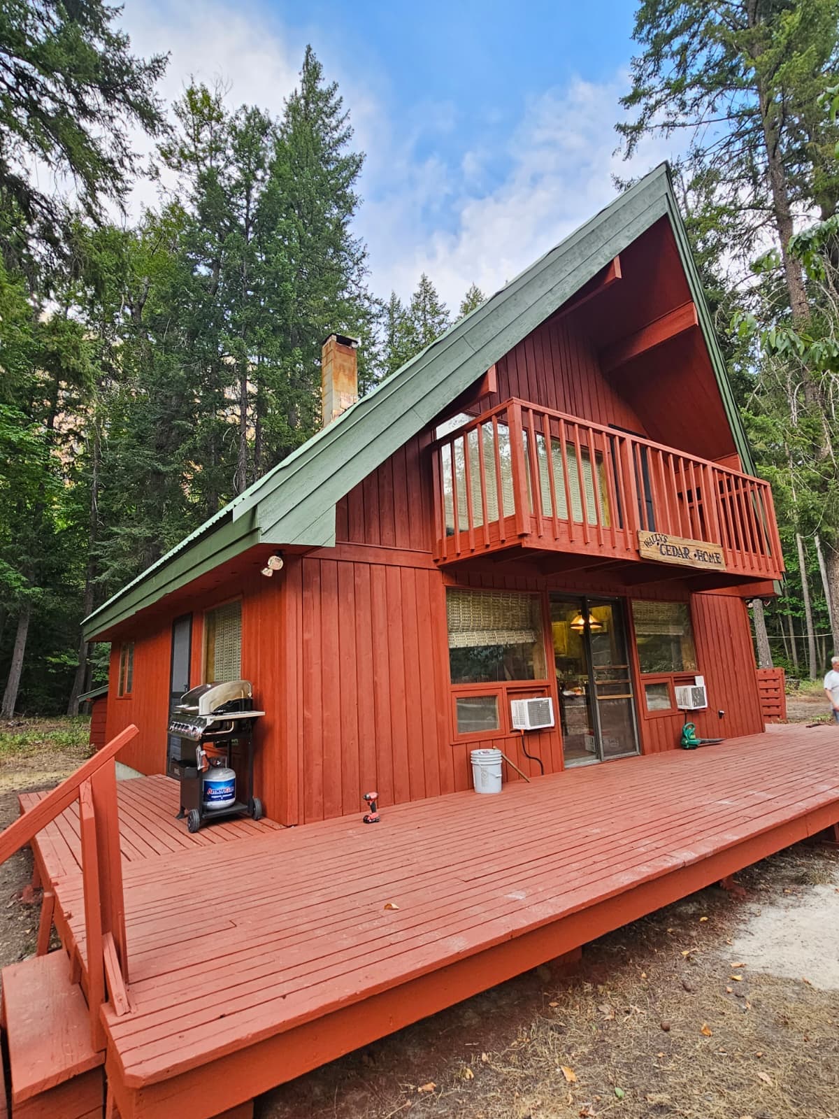 Red A-frame cabin with a freshly painted exterior and matching deck, surrounded by evergreens