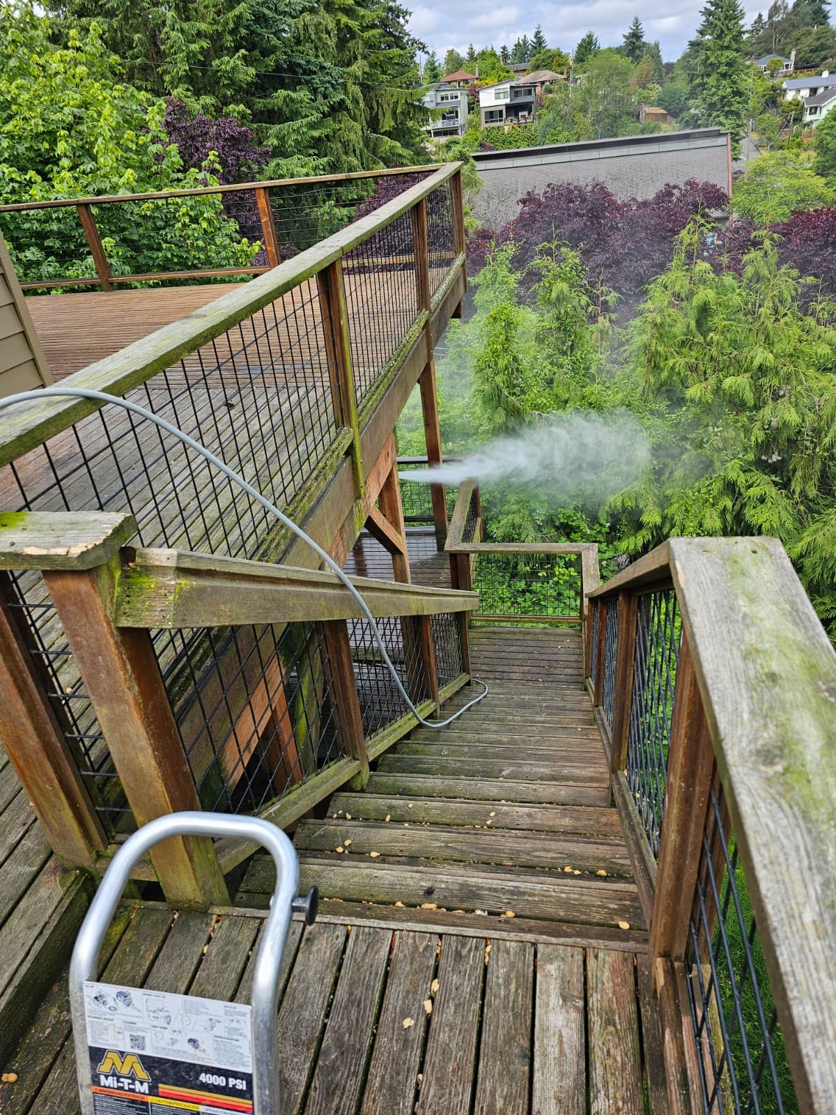 Crew pressure-washing a weathered deck and railing before staining